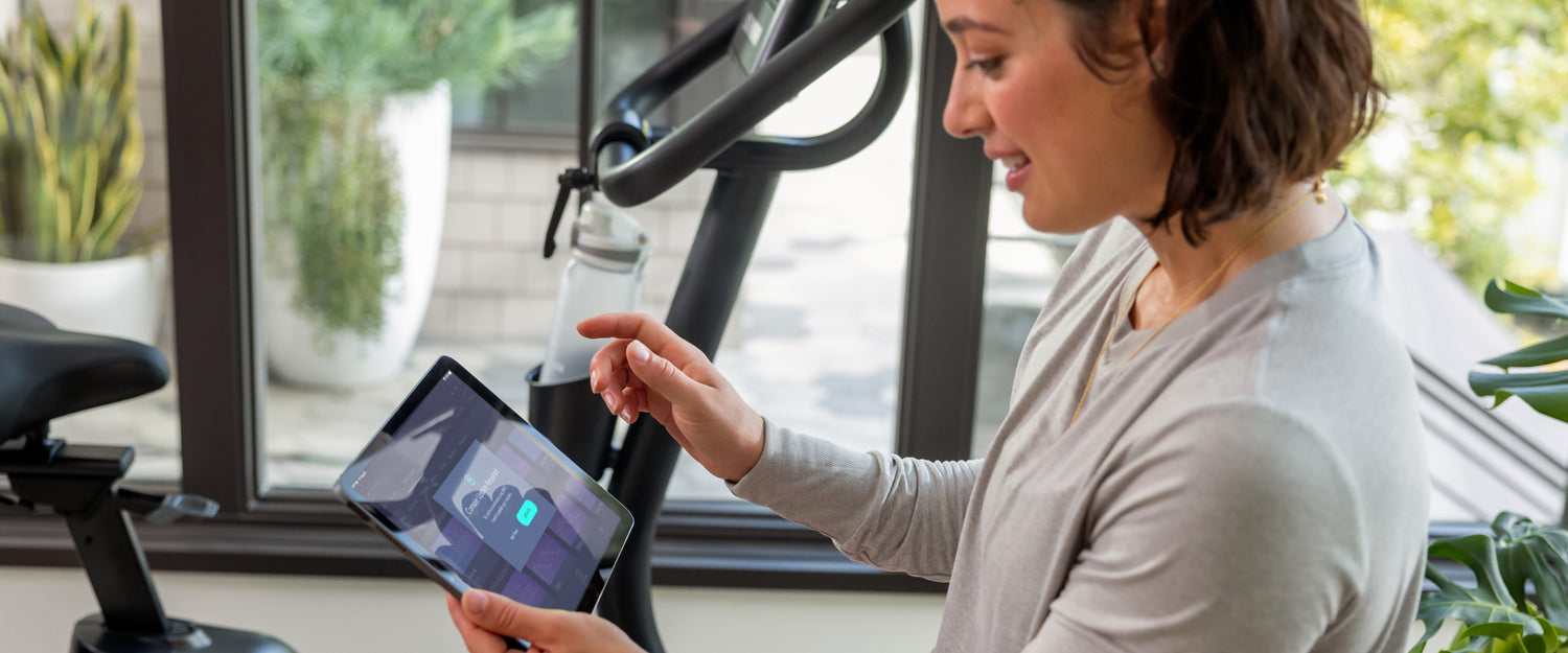 Woman looking at JRNY app screen on tablet with a Schwinn bike in the background.