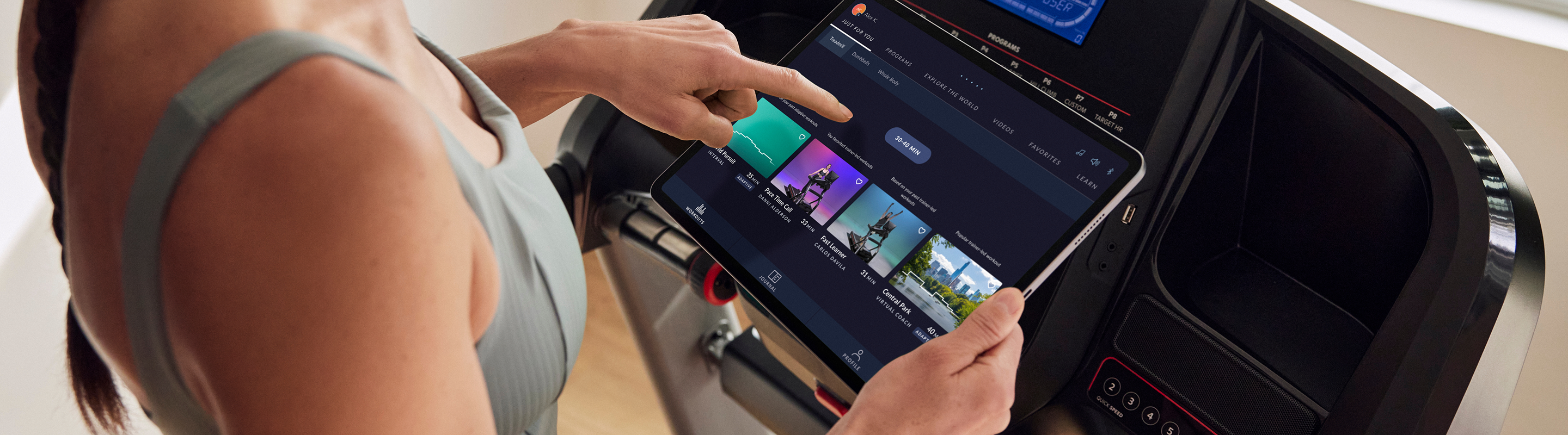 Hand tapping a tablet with the JRNY app open, with a Schwinn treadmill immediately behind it the tablet.