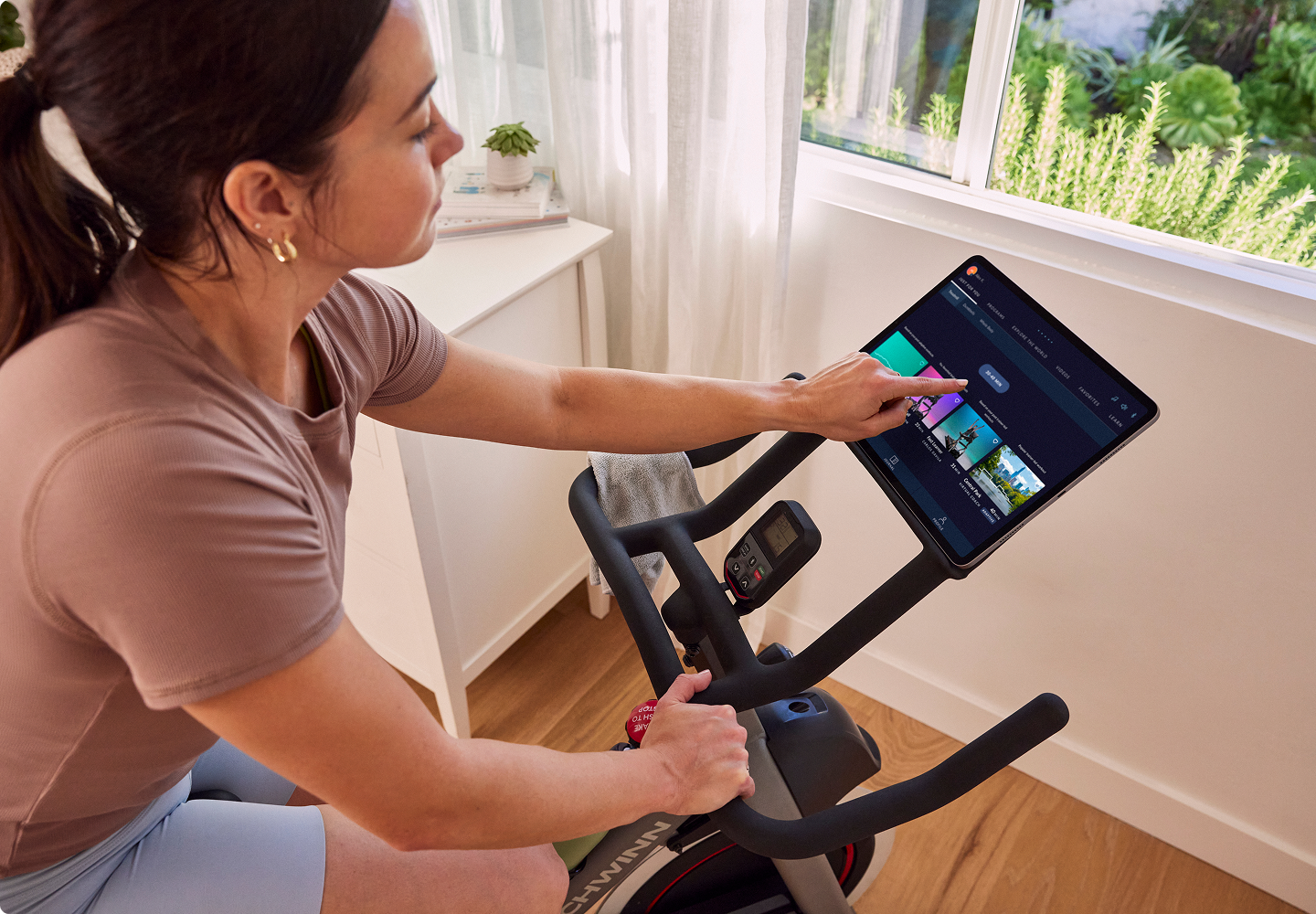 Woman using a Schwinn bike and tapping a tablet with the JRNY app displayed.